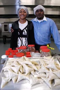 SamosaMan's founders standing behind a tray of freshly folded raw samosas in their Vermont commercial kitchen